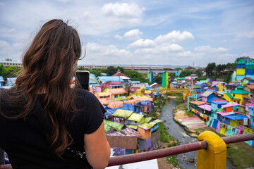 Portrait of the back of an unidentified Caucasian woman visiting Kampung Pelangi Jodipan (Malang) which has many houses with dominant colors