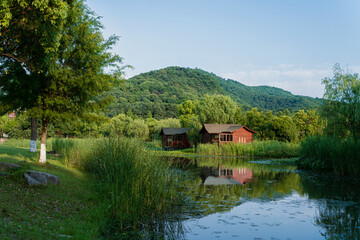 Beautiful summer landscape with wooden cabins by the lake and green mountains reflection