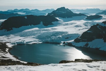 Snow-covered mountain landscape with glacial lake and distant peaks under clear sky