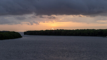 Fototapeta premium A beautiful sunset over a body of Limon river. The sky is filled with clouds, and the sun is setting in the distance. The water is calm and peaceful