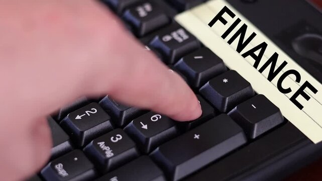 Un primer plano de un teclado con n&uacute;meros con el dedo de una mujer adulta marcado los n&uacute;meros y una nota amarilla con la palabra finanzas 