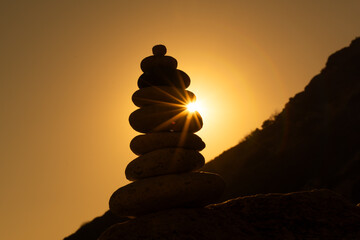 Stone stacking cairn during golden sunset on rocky coastline symbolizing balance and tranquility