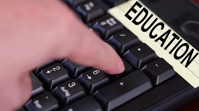 Un primer plano de un teclado con n&uacute;meros con el dedo de una mujer adulta marcando los n&uacute;meros y una nota amarilla con la palabra educacion