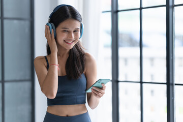 Young Asian Sportswoman in Sport Clothes Using Headphones and Smartphone After Workout at Home for Healthcare Wellness Lifestyle.