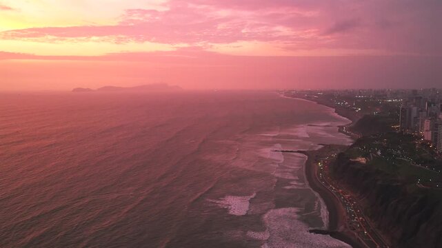 Afterglow sunset Miraflores coastal seaside aerial drone harbor Lima Peru cars traffic Makaha Barranco beach pink purple clear skies hazy cityscape skyscraper buildings ocean waves static shot
