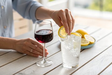 a person's hand gently pushing away a glass of red wine and reaching for a glass of clear sparkling water with lemon instead