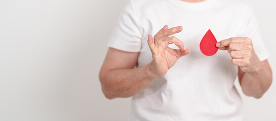Elderly woman with red Blood drop paper for concept of June World Blood Donor day, Donation, January Blood donor awareness month, April Hemophilia awareness day, May Thalassemia Day, Anemia awareness