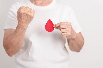 Elderly woman with red Blood drop paper for concept of June World Blood Donor day, Donation, January Blood donor awareness month, April Hemophilia awareness day, May Thalassemia Day, Anemia awareness
