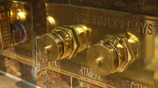 Golden brass standpipe valve closeup, polished connector mounted on tiled wall, reflective surface, embossed lettering, warm lighting, decorative industrial aesthetic, maintenance free appearance