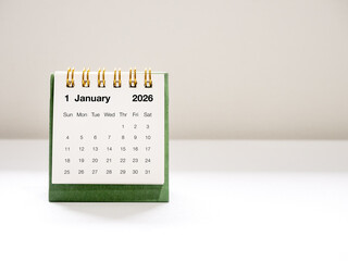 Minimal green desk calendar showing January 2026 page, with clean background and soft lighting....