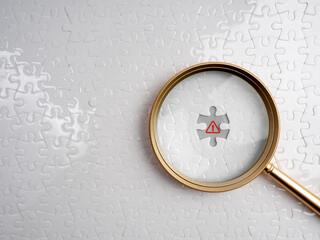 Magnifying glass highlighting red warning symbol on white missing puzzle piece, representing detection of scam, malware, or hidden threats in cybersecurity and digital investigation.
