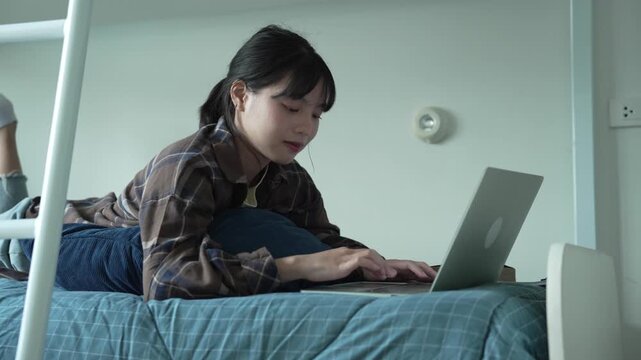 Asian girl prone on bed and typing on laptop