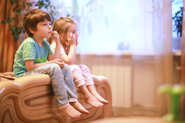 Children play construction set sitting on the sofa and watch cartoons on TV.