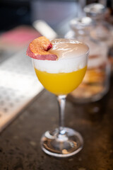 Alcoholic drink. Aperitif glass. Bright yellow tasty juice cocktail with white foam layer garnished with aromatic dried fruit slice.