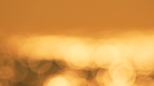 Golden bokeh shimmering water surface abstract warm background texture.