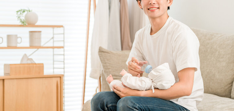 Father feeding baby with a bottle on the sofa at home, baby, infant - Powered by Adobe