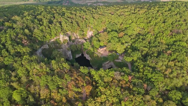 Aerial view of Tarn of Megyer-hegy near S&aacute;rospatak, Hungary, revealing lush greenery, tranquil waters, and historic millstone quarry formations in a picturesque nature preserve.