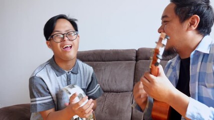 Joyful son with Down syndrome sings along to music played by father on his ukulele indoors