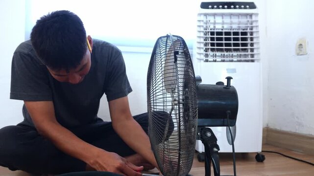 Focused man repairing standing fan indoors for home improvement and maintenance needs to keep cool