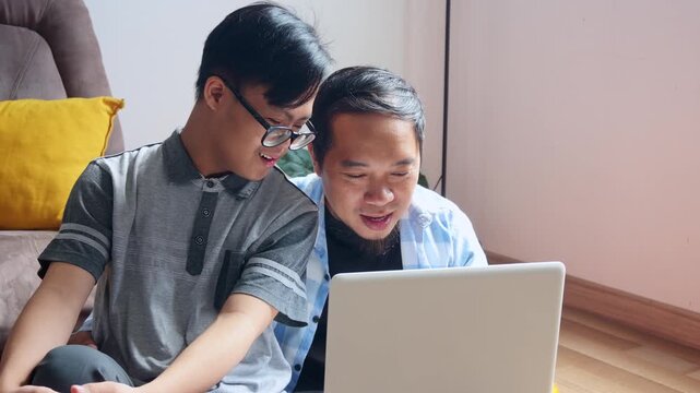 Loving father helping son with Down syndrome learn new skills using laptop at home
