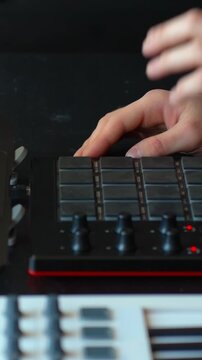 Musician's hands pressing pads on a drum machine and MIDI drum ontroller, creating electronic music beats and rhythms for production in extreme close up, dynamic studio setting, vertical shot
