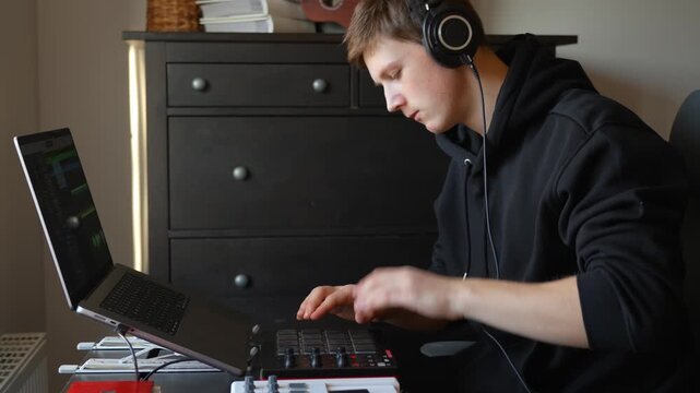 Musician playing a MIDI drum pad controller while producing music at home.