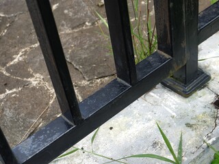 Detailed close-up of a black metal fence base contrasting with rough stone pavement and weathered concrete, highlighting urban and industrial textures.