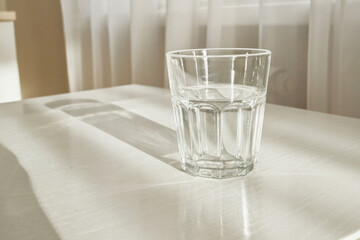 Clear glass of clear water on minimalist table with window light and shadow