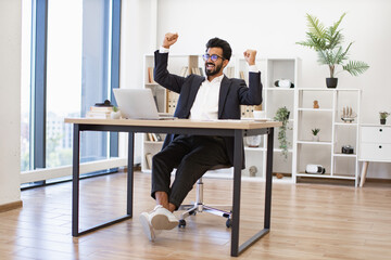 An Indian businessman celebrates a victory in his modern office, expressing joy and achievement