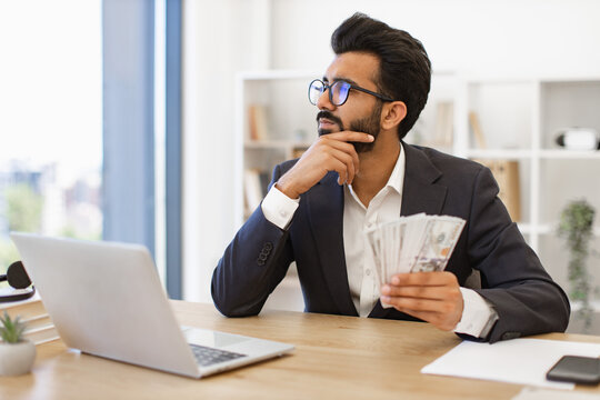 An Indian businessman contemplates his financial success while holding a stack of cash
