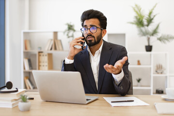 An Indian businessman in a suit gestures while talking on the phone in his office
