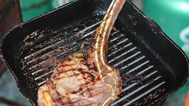4K juicy tomahawk steak is being grilled on cast iron pan.