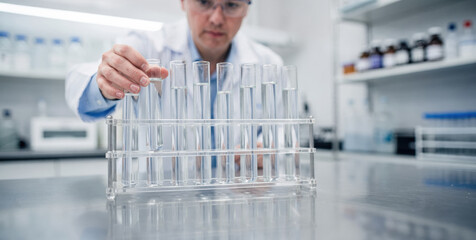 Focused male scientist in modern laboratory holding test tube. His research and analysis of clear liquid helps develop new water purification technologies for scientific breakthrough