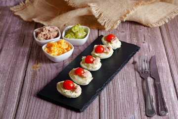 Deviled eggs arranged on a slate plate, filled with tuna mousse and topped with cherry tomatoes, served as an appetizing hors d'oeuvre