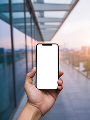 Hand Holding Smartphone with Blank Screen Against Modern Glass Building at Sunset