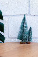 Minimal Christmas decoration with small artificial pine trees on wooden table and white brick wall background, festive holiday and winter concept.