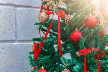 Festive Christmas tree decorated with red ribbons, gold and red ornaments, pinecones, and warm holiday light against a brick wall background.