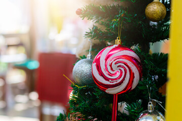 Close-up of a colorful lollipop ornament hanging on a Christmas tree with festive decorations, warm light, and holiday atmosphere.