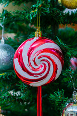 Close-up of a colorful lollipop ornament hanging on a Christmas tree with festive decorations, warm light, and holiday atmosphere.