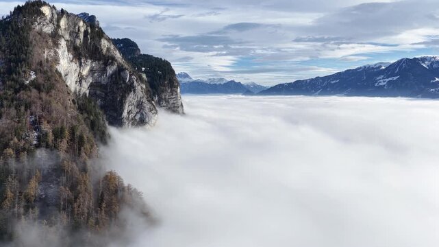 steep Swiss cliffs rise above a glowing cloud ocean facing distant snowy peaks