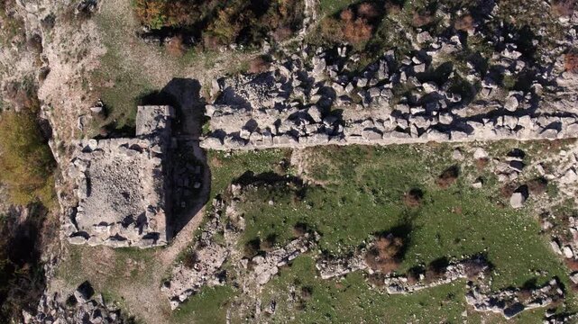 Straight-down aerial shot of the Daorson archaeological site near Stolac, revealing the layout of ancient Illyrian stone structures, walls, and surrounding terrain in clear autumn light.