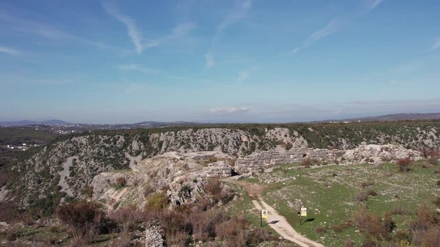 Aerial view of the ancient Daorson Illyrian fortress near Stolac, showing massive stone walls and a wide plateau surrounded by rugged hills and clear sky, captured in bright daylight.
