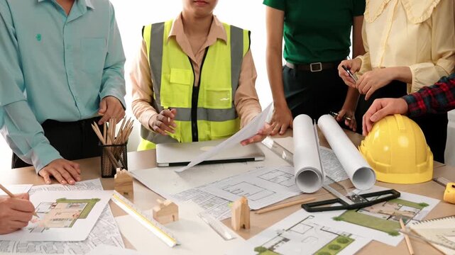 Smart architect and safety engineer discussion about building blueprint on table with architectural document, measurement tools and wooden block scatter around at modern office. Closeup. Delineation.
