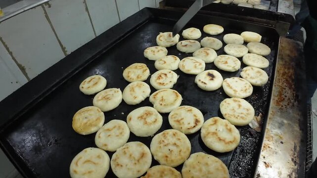 Dolly out tracking shot of hands placing raw Venezuelan arepas on a hot griddle for cooking.