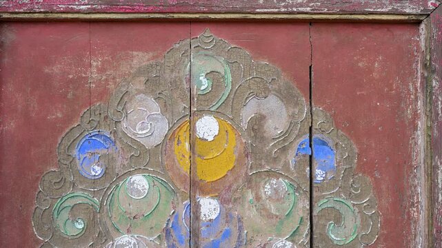 Close-up of ancient painted wood detail at Erdene Zuu Monastery in Kharkhorin, Mongolia. The weathered red surface features faded traditional Buddhist patterns, highlighting historic artistry.