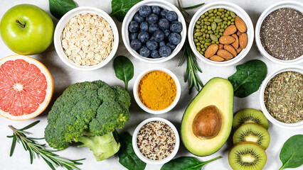 Assorted healthy foods including fruits, vegetables, nuts, seeds, and spices arranged on a white surface