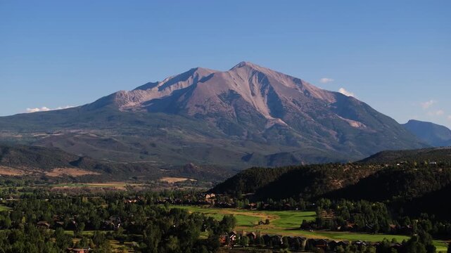 Sunlit Mount Sopris slopes glow warmly above green valleys in a wide Colorado mountain panorama, establishing static