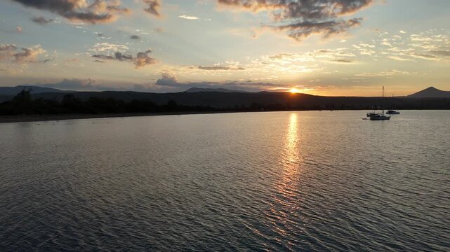 Navarin,Messinia,Aerial view forward from Giolova Beach towards the mountains during sunrise.Beautiful panoramic scenery of mountains and clouds,reflection of the sun over sea.