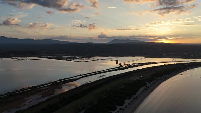Navarin,Messinia,Aerial birds eye view circle pan left from Giolova Beach towards Gialova Lagoon during sunrise.Beautiful panoramic scenery of mountains,reflection of clouds over the lagoon.