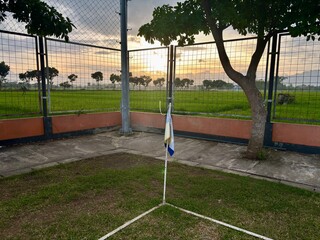 Corner flag on an empty soccer field during sunset. Calm sports ground with green grass, fence, and warm evening light. © Ilhamdh